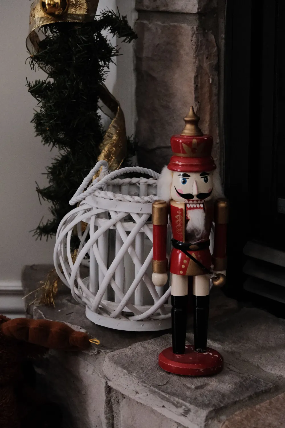 Traditional nutcracker doll next to a festive white lantern and garland by a fireplace.