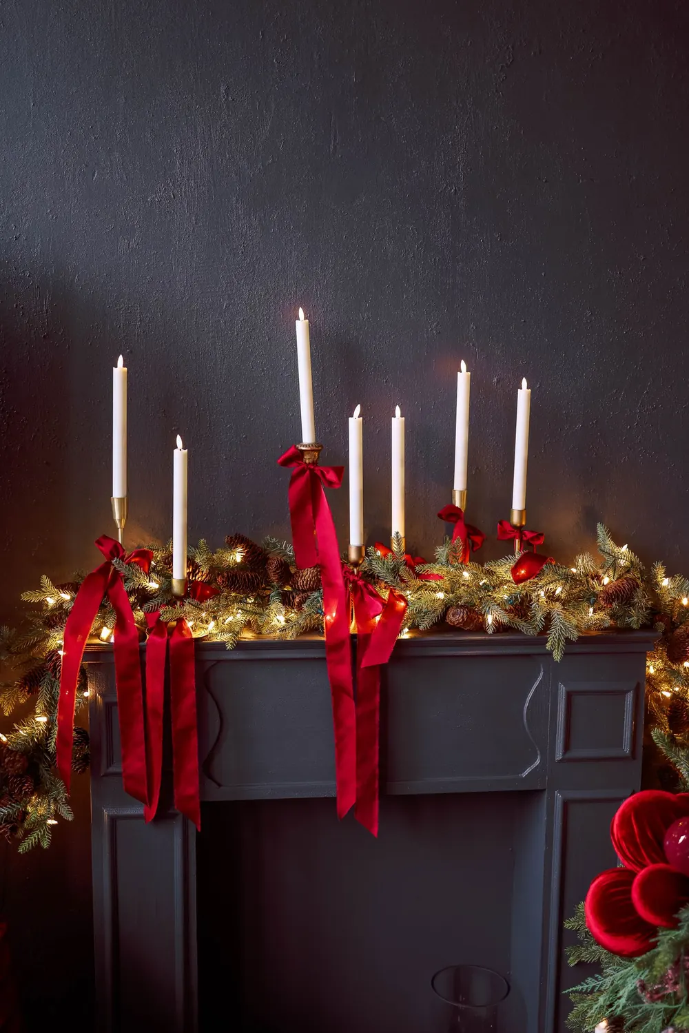 Festive Christmas mantel decorated with candles, red ribbons, and greenery for a cozy holiday atmosphere.