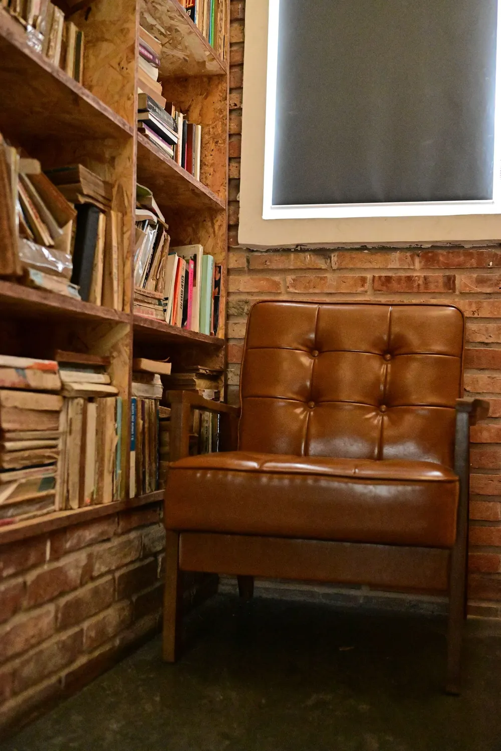 A cozy corner with a vintage leather armchair and a wooden bookshelf filled with books.