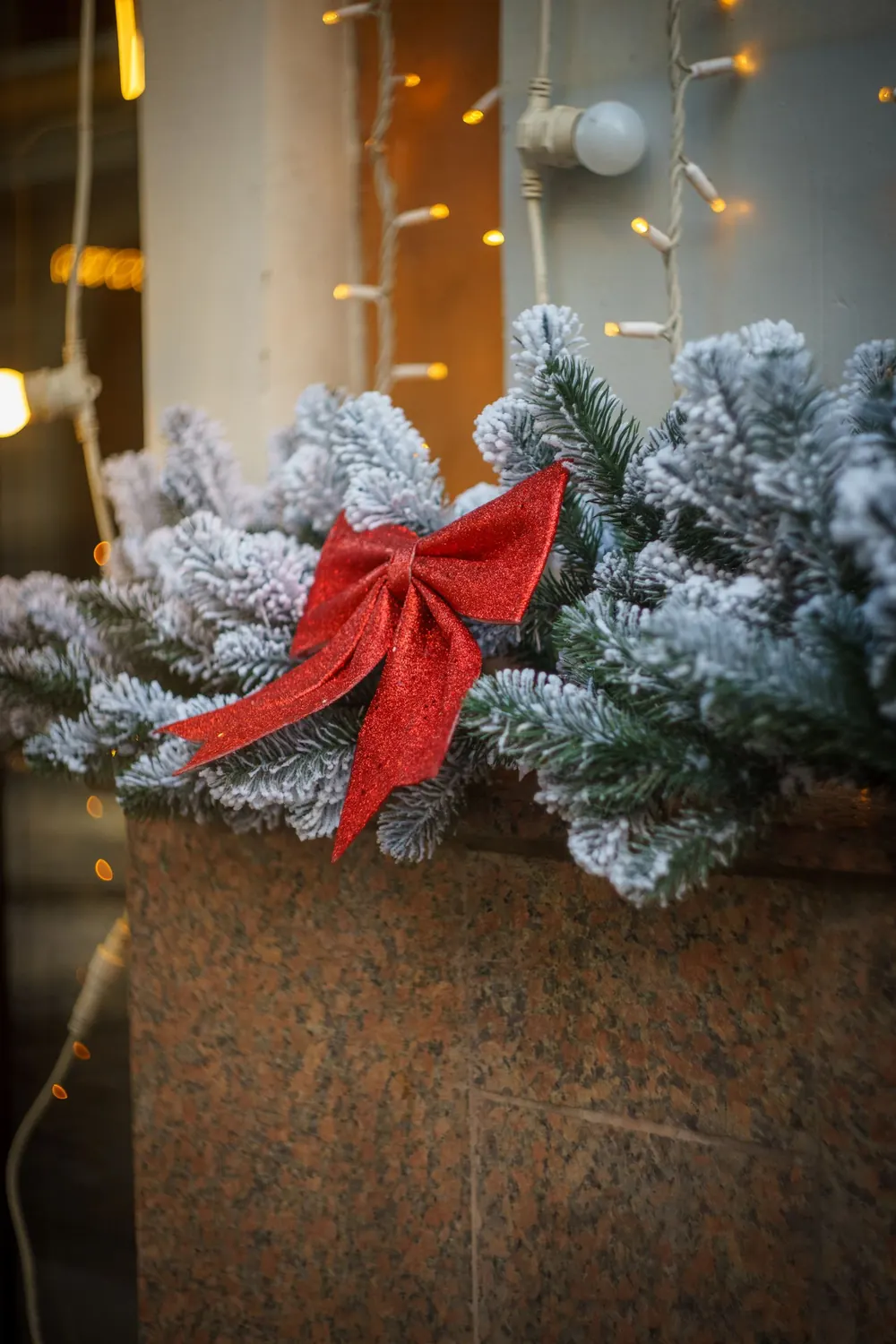 A festive garland with a red ribbon and snow-covered evergreens, perfect for holiday decor.